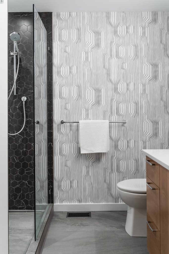 Modern bathroom with glass shower, wooden cabinetry and geometric patterned wallpaper