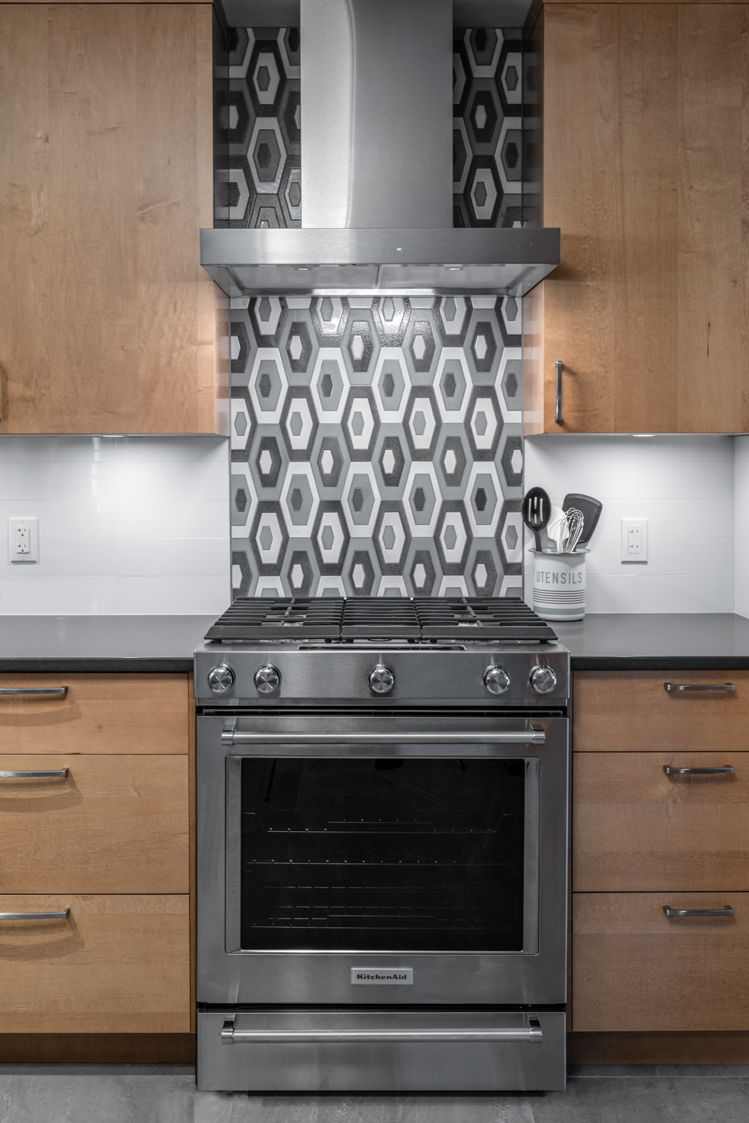 Modern kitchen with wooden cabinetry, stainless steel gas range, and vintage-inspired geometric patterned stove backsplash