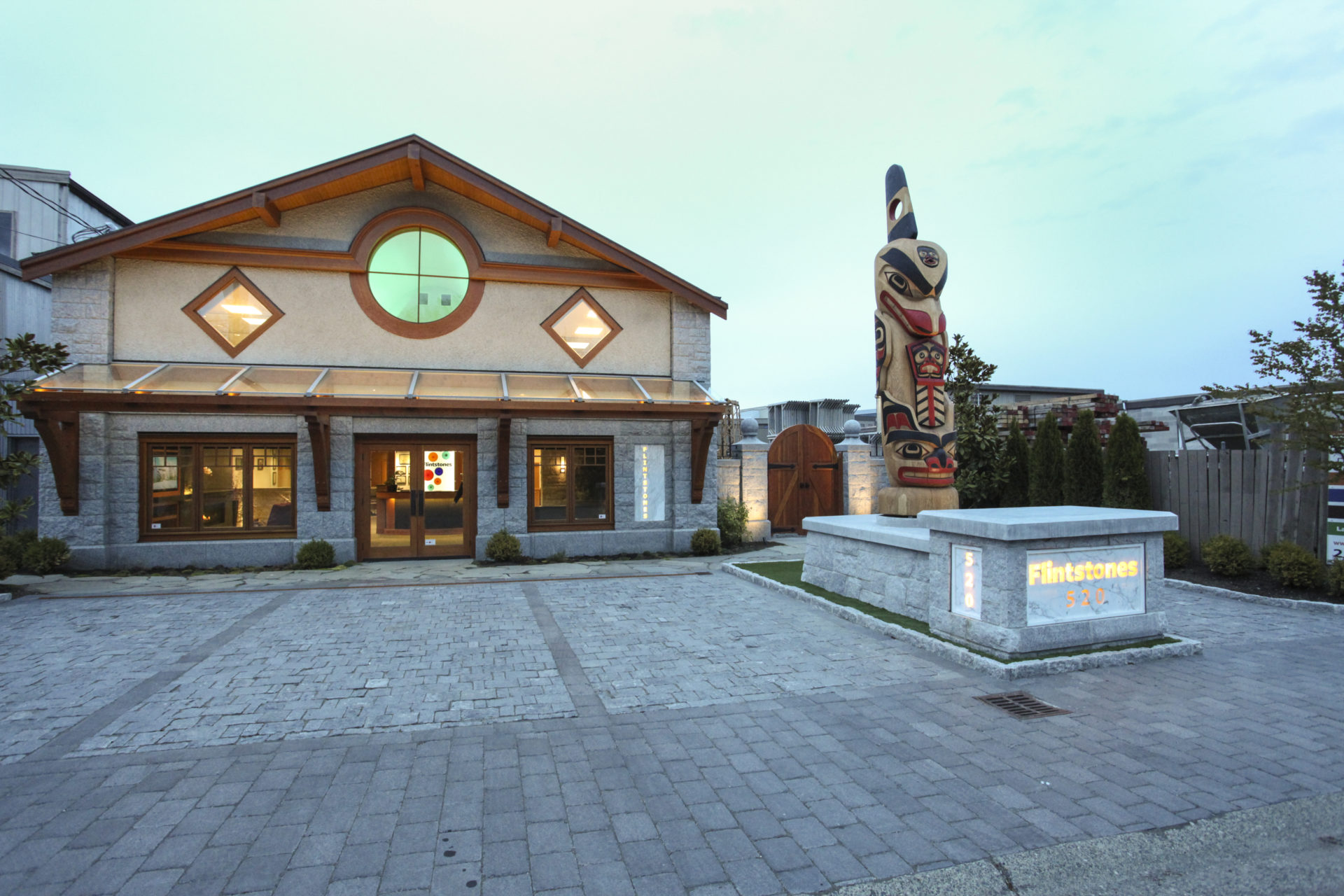 Two-level building with large stone driveway, glass awning, and totem pole