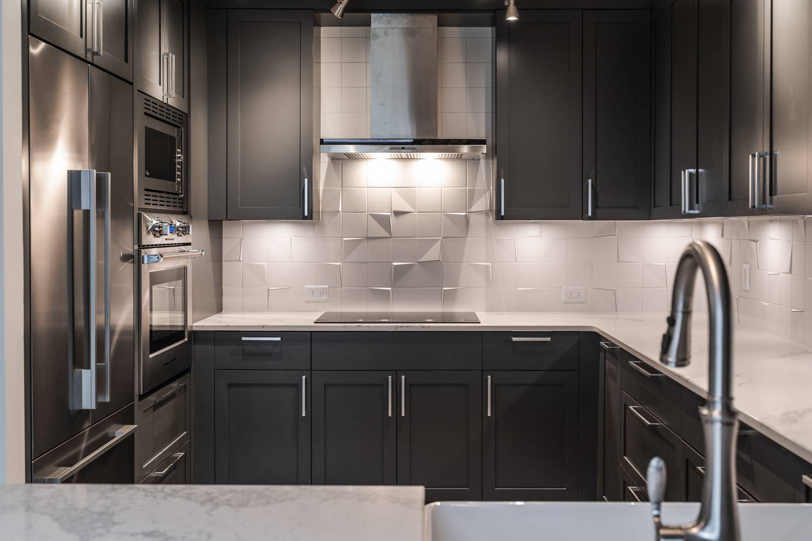 Modern kitchen with dark cabinets, marble countertops, and unique backsplash featuring projecting tile corners